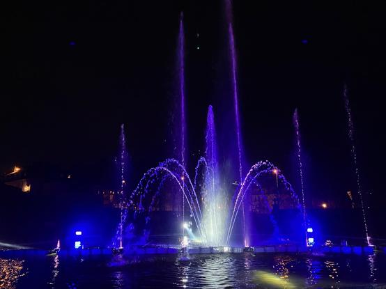 An illuminated water fountain. The water streams are dancing to the music playing.
